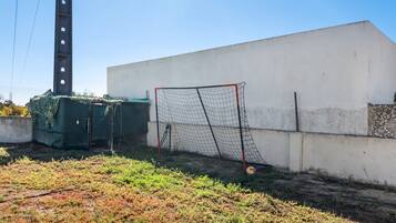 Un but de football situé dans un espace délimité par une clôture, avec un mur blanc et une structure recouverte d’une bâche verte.