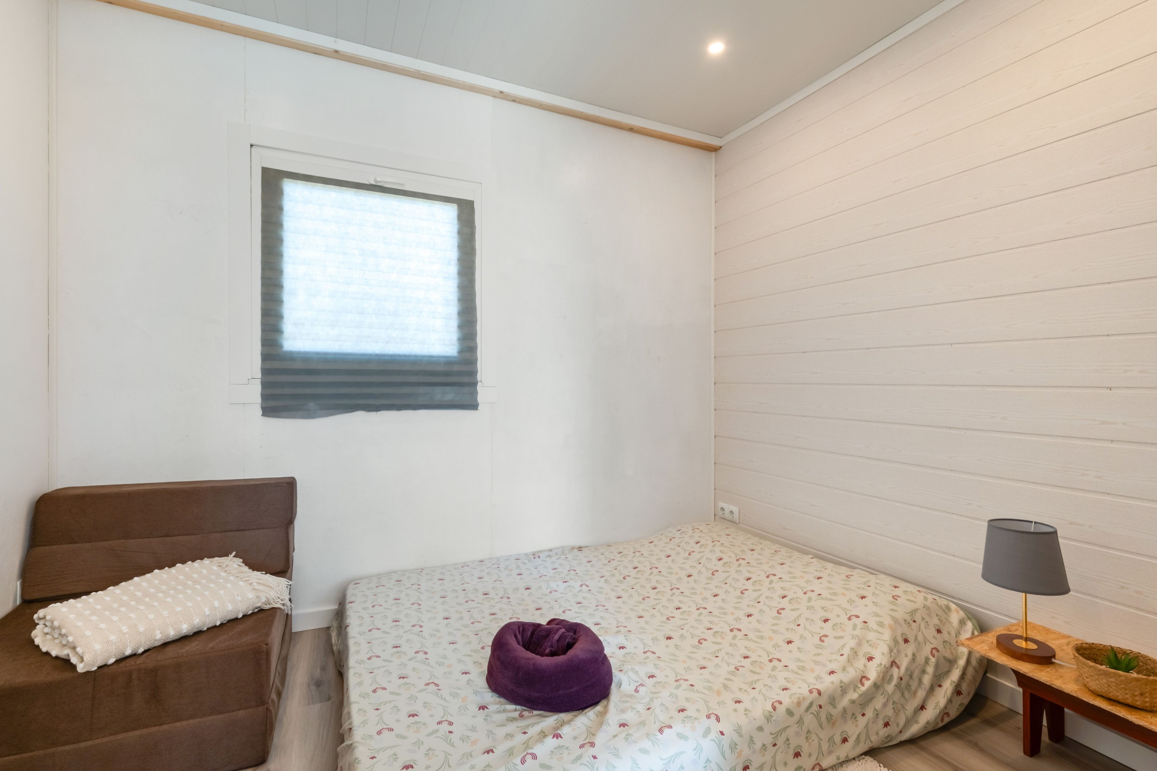 Una habitación con una cama, una silla, un ventanal y una lámpara.