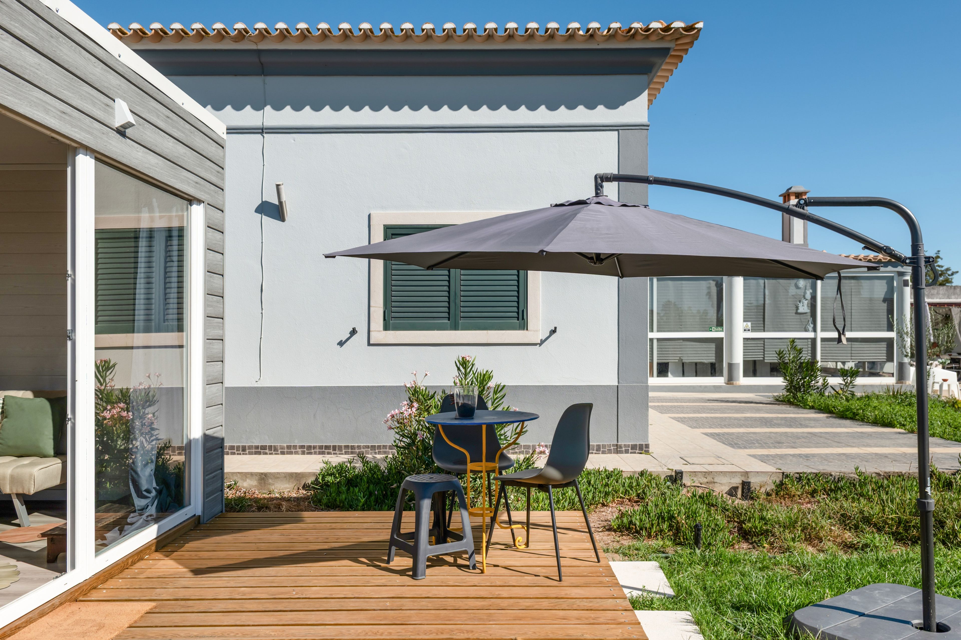 Een terras met een tafel, stoelen en een grote parasol, plus een houten vlonder.