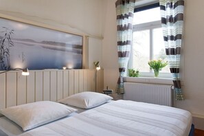 Quarto com cama, janela com cortinas, radiador e quadro pendurado na parede.