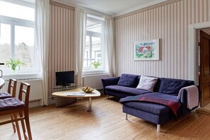 A living room with a sofa, a television, a coffee table, and a window with curtains. - Holiday apartment with 2 bedrooms (Groß Zecher)