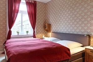 A bedroom with a large bed, a nightstand, a wooden cabinet, and a window with curtains. - Holiday apartment with 2 bedrooms (Groß Zecher)