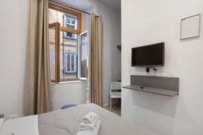 A hotel room with a bed, a TV mounted on the wall, a window with curtains, and a chair. - Double Room with Wi-Fi and Air Conditioning (Napoli)