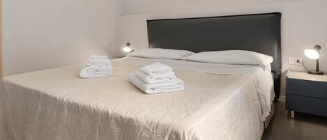 A neatly made bed with a quilted bedspread, two bedside lamps, and a framed picture on the wall.