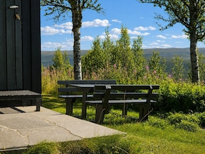 A wooden bench with a stone ledge, surrounded by greenery and trees, overlooking a hilly landscape. - Hvilebu - Charming and Traditional Cabin at Kikut, Geilo (Hol)