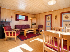 Een gezellige kamer met een houten vloer, een zithoek, een eettafel en een open haard.