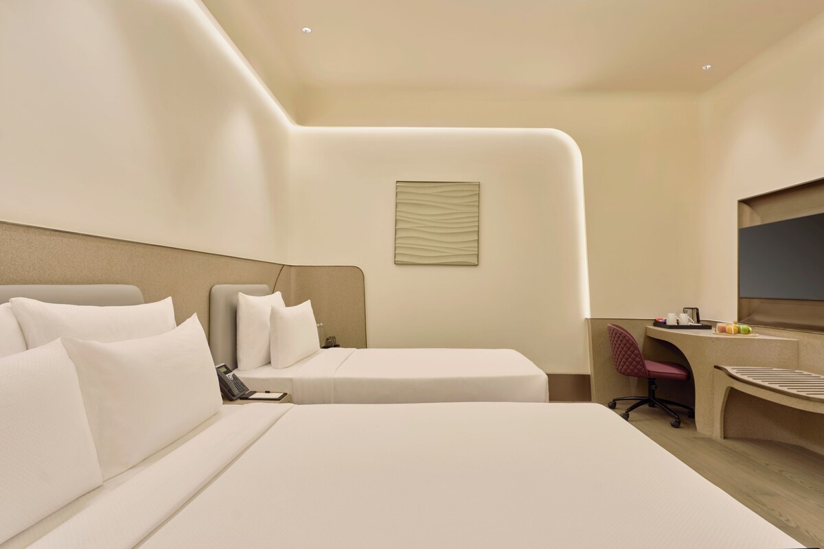 A hotel room with two beds, a desk, a chair, a telephone, and a flat-screen TV.