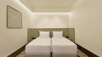 A hotel room with two beds, a nightstand, a phone, and a wall-mounted light fixture.