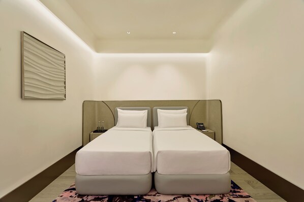 A hotel room with two beds, a nightstand, a phone, and a wall-mounted light fixture. - Swirl Transit Hotel by Adani (Panvel)