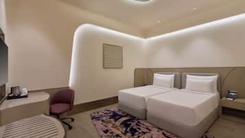 A modern hotel room with a double bed, a small desk, a chair, and a patterned rug.