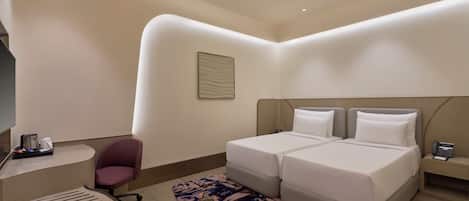 A modern hotel room with a double bed, a small desk, a chair, and a patterned rug.