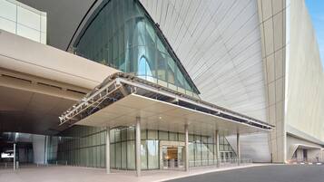 A modern building with a curved glass facade, a covered entrance area, and a clear sky.
