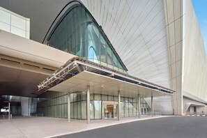 A modern building with a curved glass facade, a covered entrance area, and a clear sky. - Swirl Transit Hotel by Adani (Panvel)