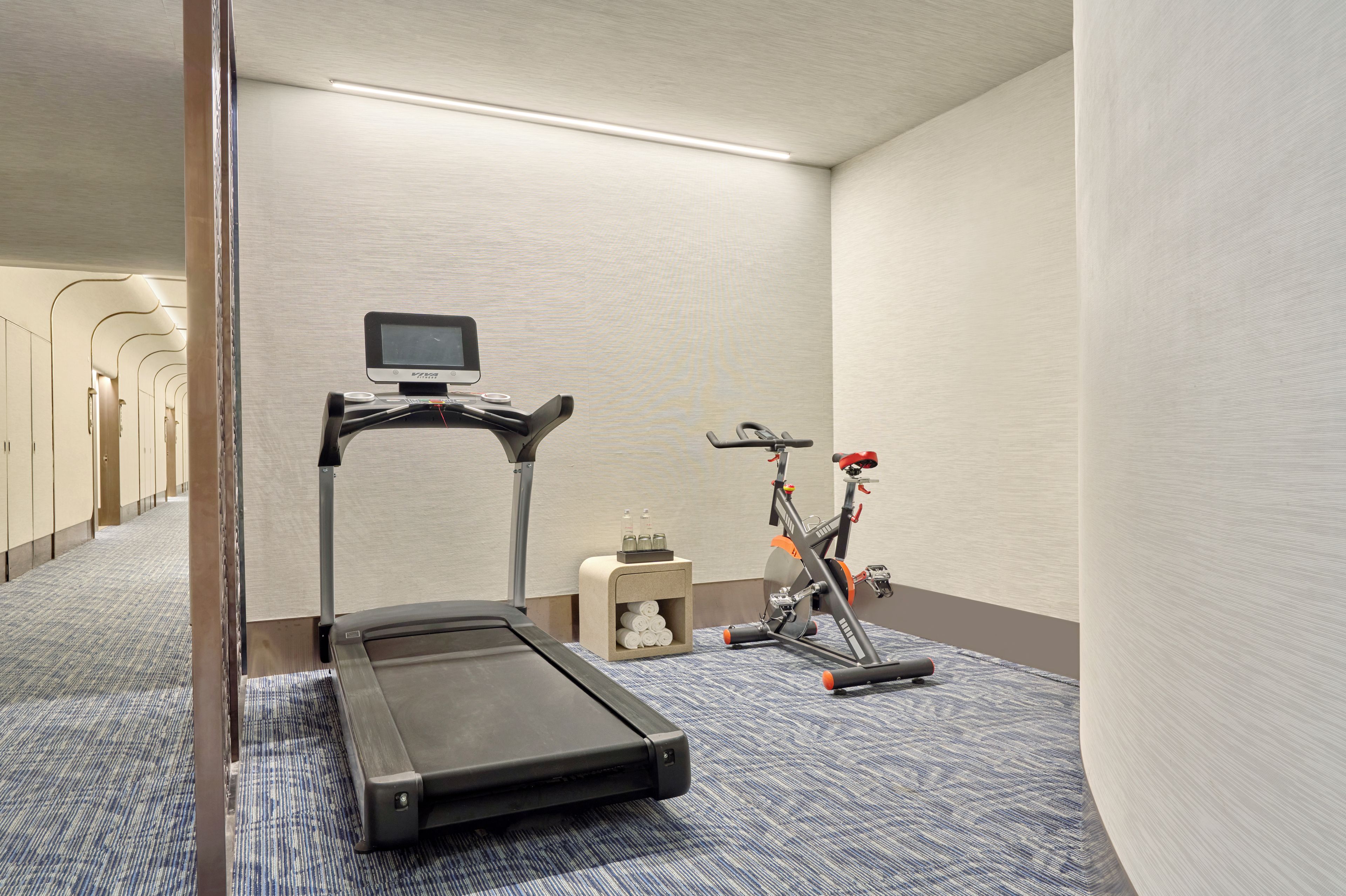 Habitación de hotel con una cinta de correr, bicicleta estática y una pequeña mesa con artículos de aseo.