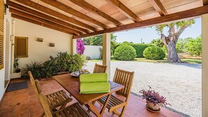 An outdoor patio with a wooden table and chairs, surrounded by potted plants and a view of a garden. - Rustic Country Villa With Private Pool (Pollença)