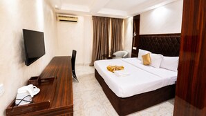 Quarto de hotel com cama, escrivaninha, cadeira, televisão e janela com cortinas.