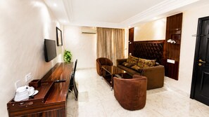A hotel room with a wooden dining table, a sofa with patterned cushions, a brown armchair, and a black door. - Starview Palace Abuja (Gwarinpa)