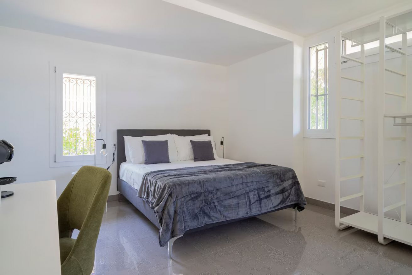 Una camera da letto con un letto, una scrivania, una sedia, un armadio e una finestra con inferriata.