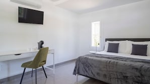 Ein Schlafzimmer mit einem Bett, einem Schreibtisch, einem Sessel, einem Fernseher und einem Fenster.