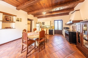A dining area with a round table and chairs, a kitchen with modern appliances, and a wooden ceiling.