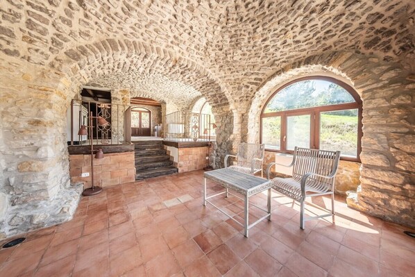 An interior with stone walls, a staircase, and a seating area with chairs and a table.