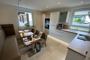 A modern kitchen with a dining area, built-in appliances, and large windows. - HarzVilla Bad Sachsa. (Bad Sachsa)