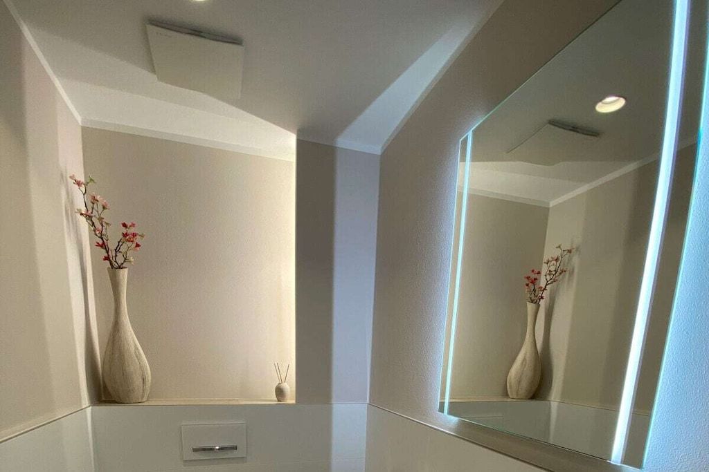Une salle de bain moderne avec un grand miroir, deux vases de fleurs et un interrupteur.