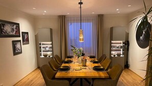 En matplats med ett träbord dukat för sex personer, omgivet av stolar, med en hängande lampa ovanför och en växt på bordet.
