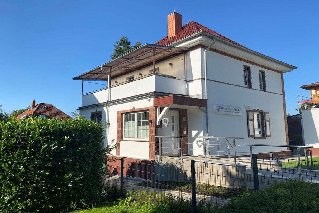 A two-story building with a flat roof, a visible entrance, and a sign indicating it is a holiday home.