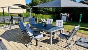 En uteplats med ett bord och stolar, en grill och en överbyggd sittplats.