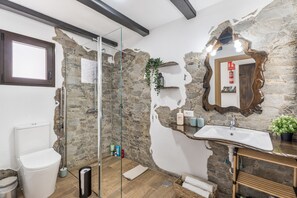 Un baño con pared de piedra, cabina de ducha de vidrio, lavabo blanco y tocador de madera.