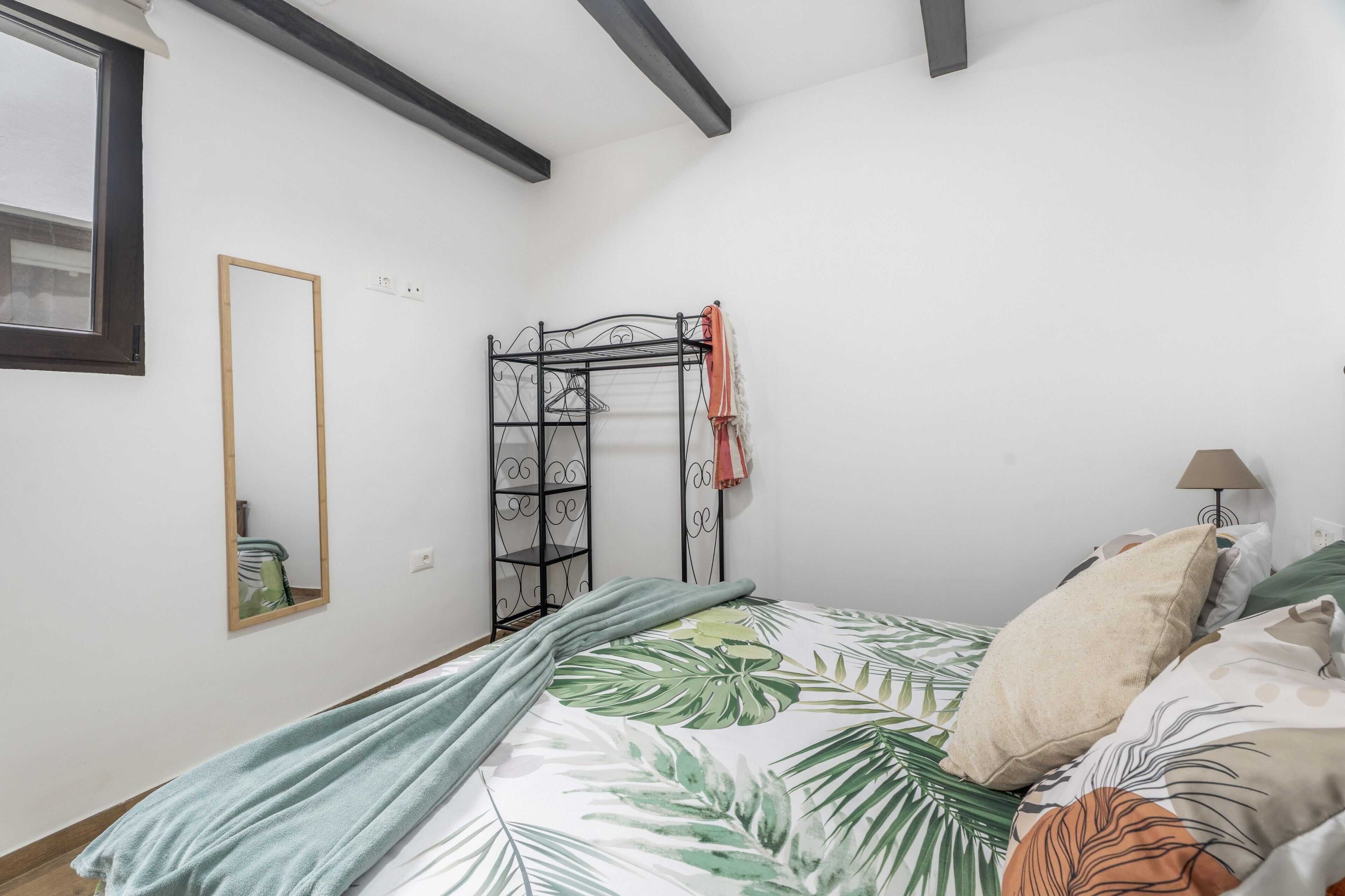 A bedroom with a bed, a hanging clothes rack, a mirror, and a lamp.