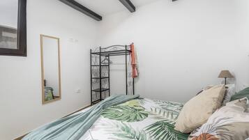 A bedroom with a bed, a hanging clothes rack, a mirror, and a lamp.