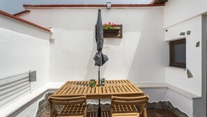 Et sæt træborde og stole på en terrasse med en hvid væg og et vindue.