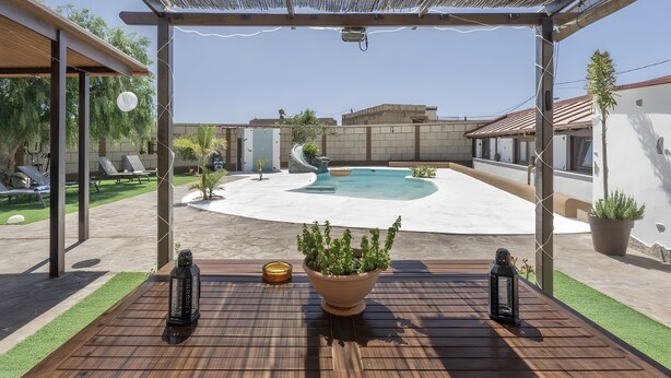 En træterrasse med en potteplante og to lanterner, med udsigt over en swimmingpool og en bygning.