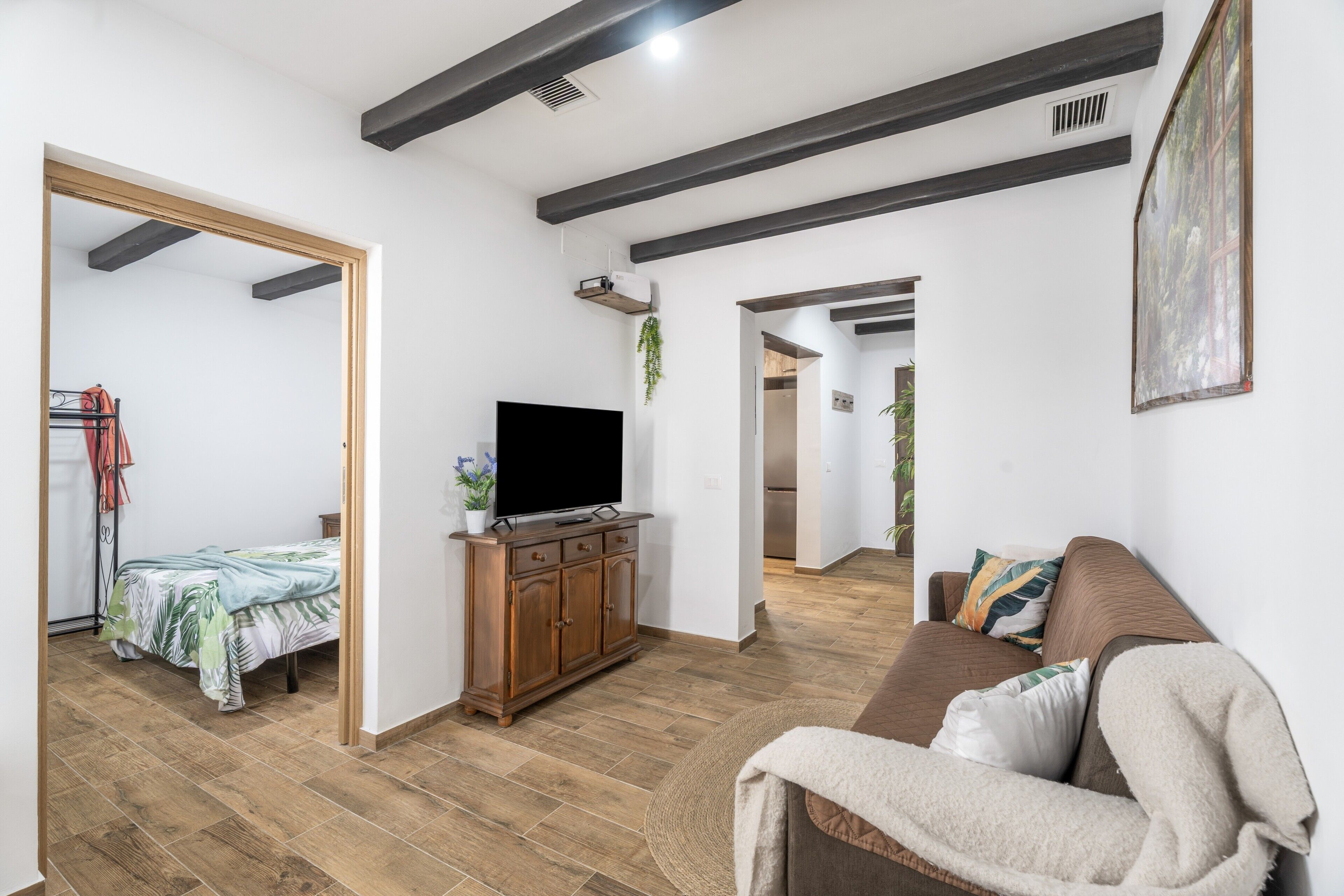 Ein modernes Wohnzimmer mit einem Flachbildfernseher auf einer Holzkommode, einer Couch mit Kissen und einem Bett mit floralem Bettbezug.