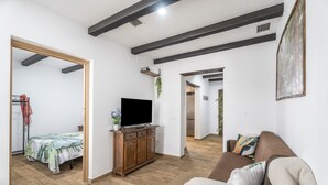 En moderne stue med et fladskærms-tv på et træskab, en sofa med puder og en seng med blomstret sengetæppe.