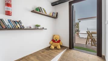 Quarto com piso de madeira, um urso de pelúcia e duas prateleiras com livros e uma pequena planta.