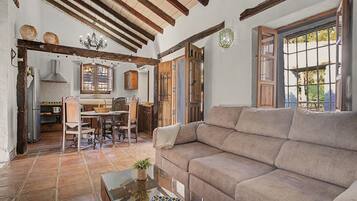Amplia sala de estar con sofá, mesa de comedor con sillas, zona de cocina con muebles de madera y un gran ventanal que proporciona luz natural.