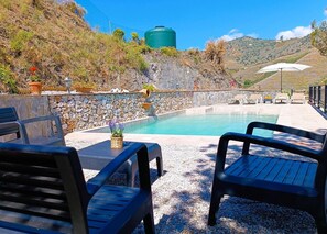 Ein Poolbereich mit Steinmauern, Sitzgelegenheiten im Freien und Blick auf Hügel.