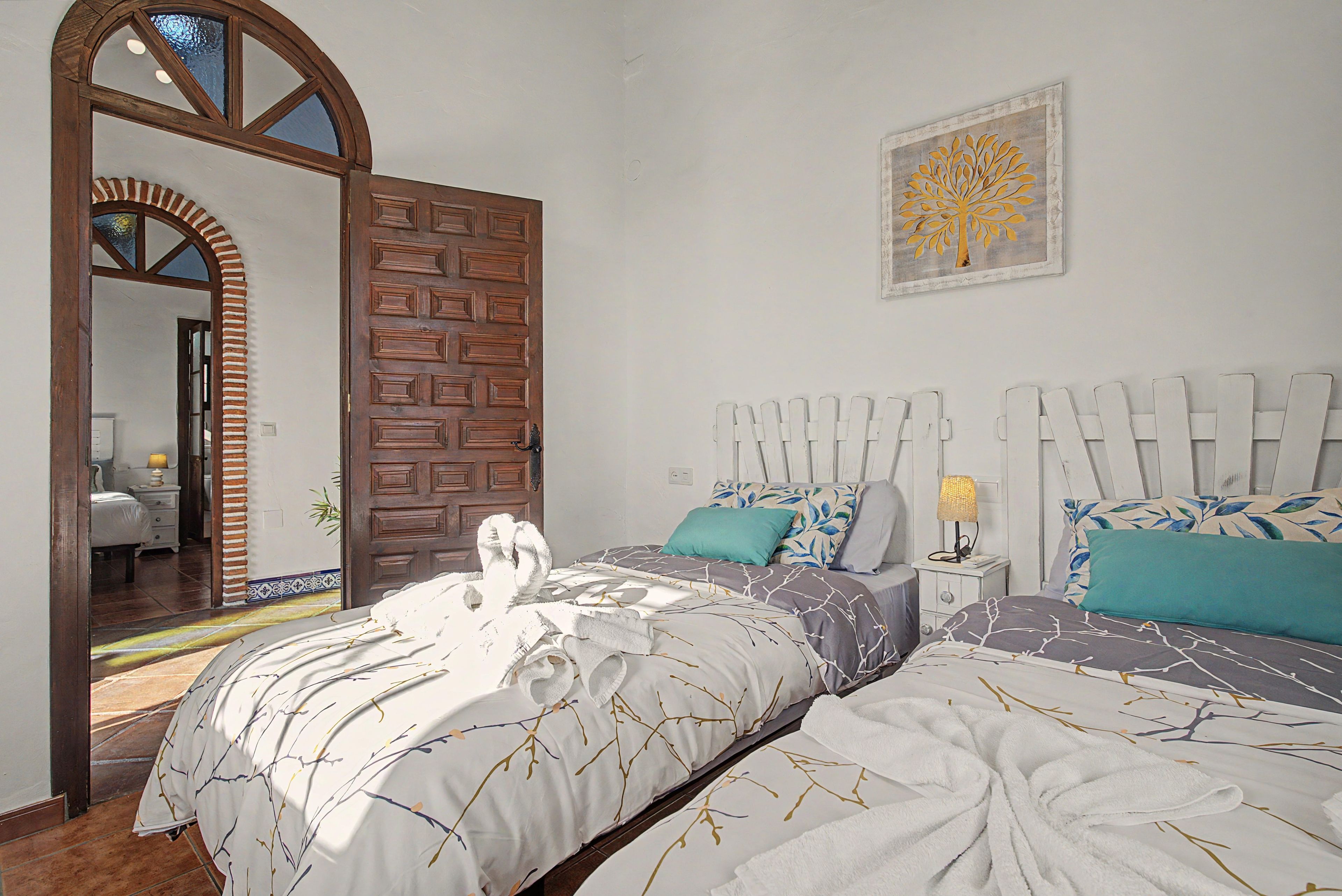 A bedroom with two beds, a wooden door, a mirror, and a wall-mounted artwork.