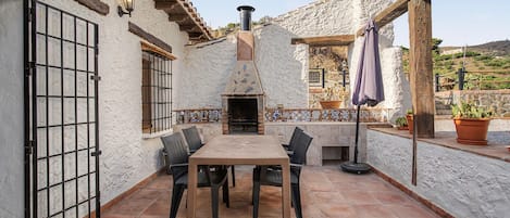 An outdoor patio with a tiled floor, a table with chairs, a chimney, and potted plants.