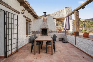 An outdoor patio with a tiled floor, a table with chairs, a chimney, and potted plants. - Cortijo Eucalipto 1 with Sea Views, Private Pool, and Air Conditioning (Nerja)