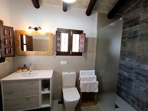 Ein Badezimmer mit einem weißen Waschbecken, einer Toilette und einer Duschkabine. Holzschränke und ein Spiegel befinden sich über dem Waschbecken.