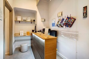 Un comptoir d’accueil avec un ordinateur, un téléphone et un panneau indiquant la présence d’une connexion Wi-Fi et le mot de passe. Des certificats sont affichés au mur, ainsi qu’un tableau d’affichage où sont accrochés divers documents.