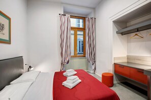 Une chambre d’hôtel avec un lit, un bureau, un miroir et une fenêtre avec des rideaux.