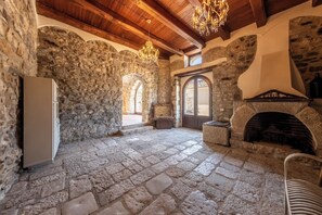 A stone-walled room with a fireplace, a chandelier, and a door leading to an outdoor area.