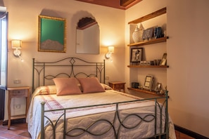 A bedroom with a metal bed frame, two bedside lamps, a mirror, and a shelf with decorative items.