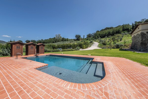 A swimming pool with a brick deck, surrounded by greenery and a stone wall.