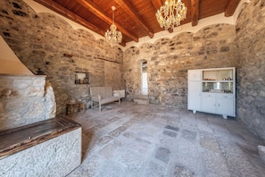 A rustic stone interior with a wooden bench, a white cabinet, and a chandelier.